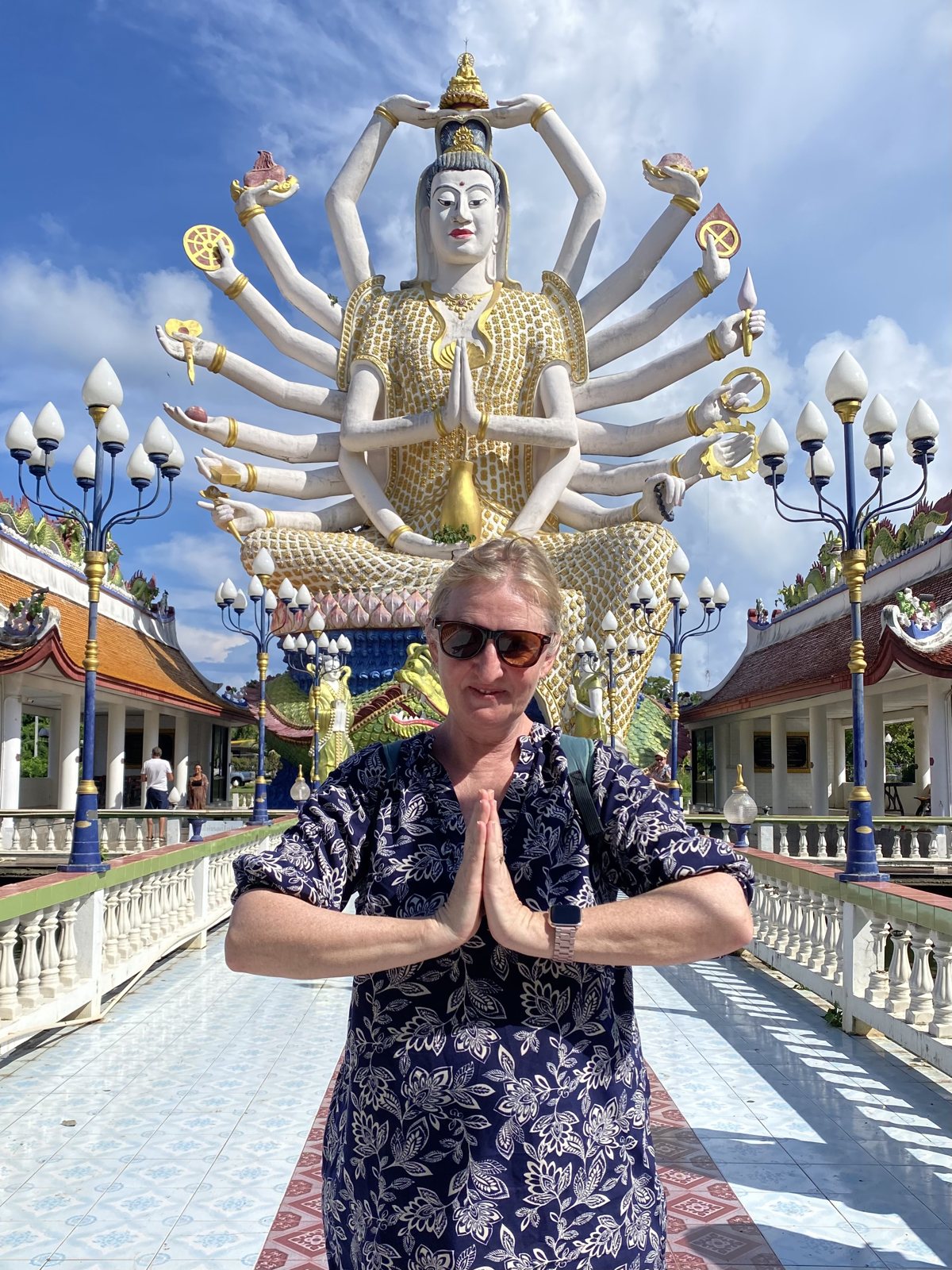Lianne Byrne, hands together, in front of a huge many-armed statue at a temple