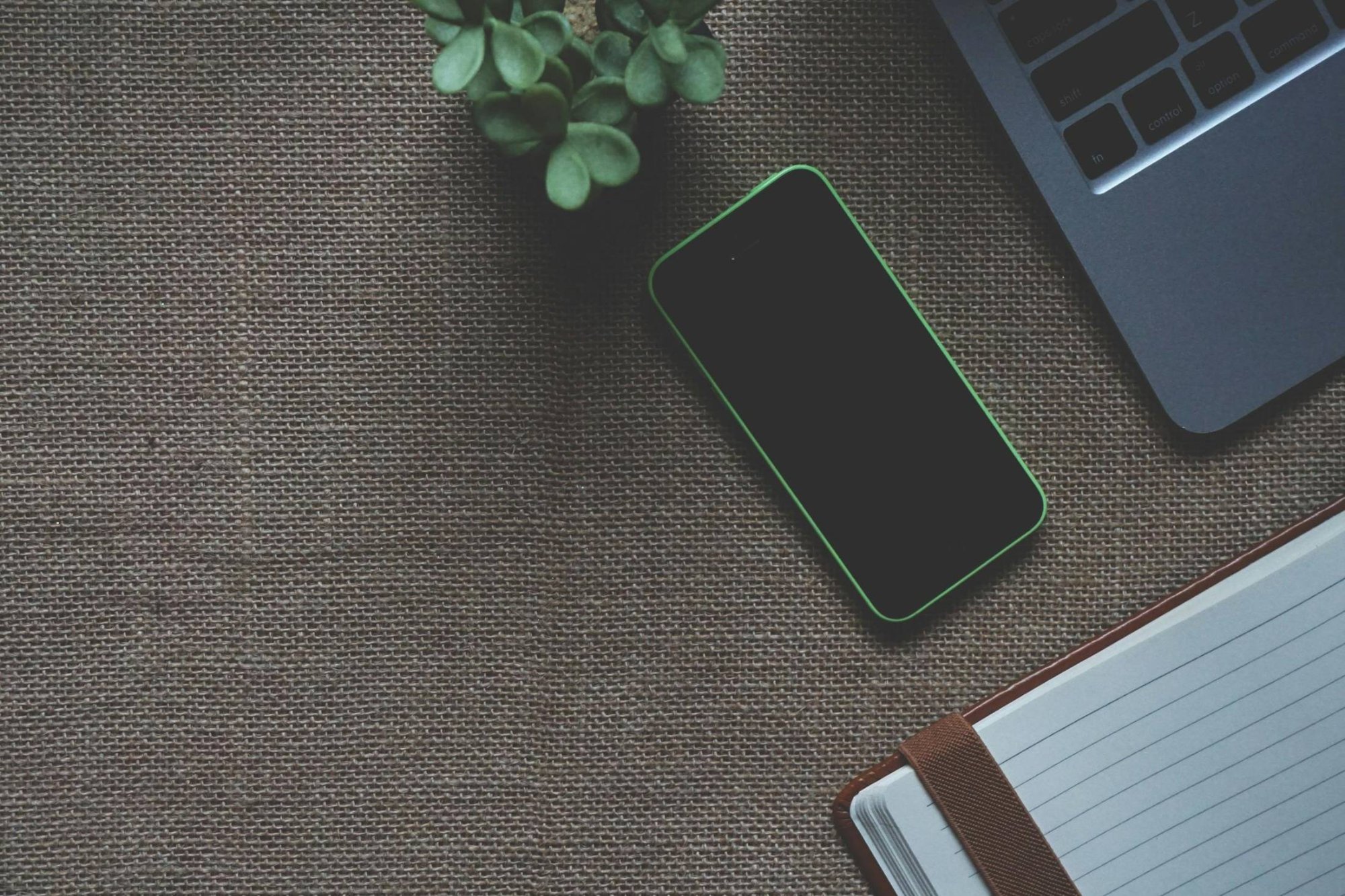 Flat lay workspace — phone, laptop, notebook and plant